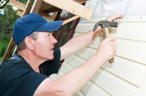 Installer securing vinyl siding panel to home exterior with hammer
