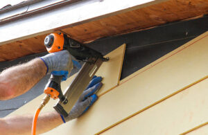 Contractor nailing fiber cement siding panel to residential home exterior