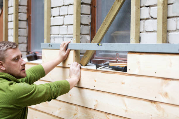 Worker installing wood siding on a residential house with a level tool